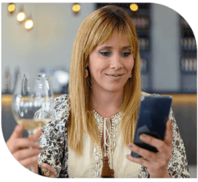 A woman holding a wine glass and looking at her phone.