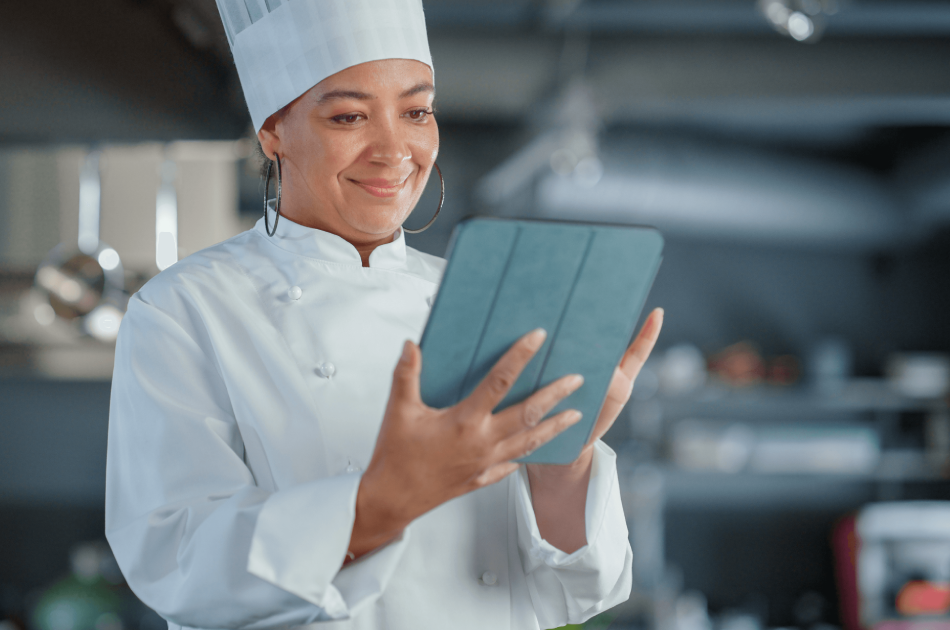 A woman in chef 's outfit holding an ipad.