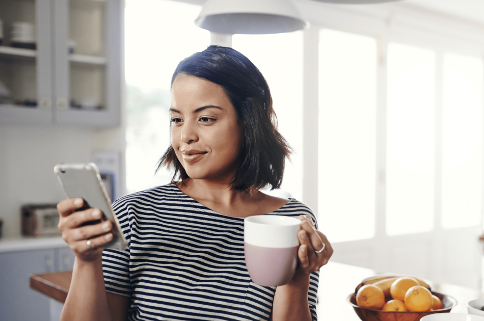 A woman holding a cup and looking at her phone.