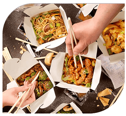 A group of people holding chopsticks over some food.